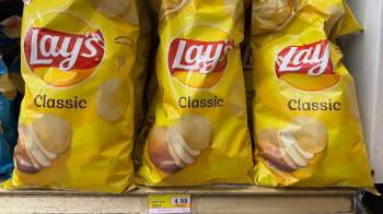 Three bags of Lay's Classic potato chips displayed on a shelf with a price tag of $4.98.