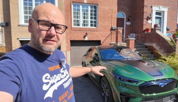 A man stands next to a green car in a residential driveway.