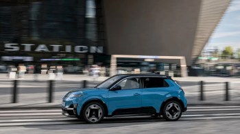 A blue car drives past a modern building with a sign that says "STATION."