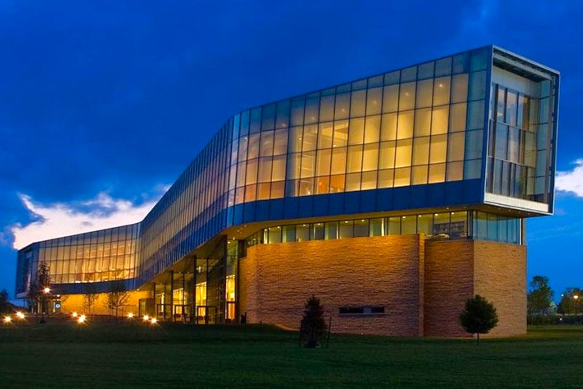 A modern building with glass walls and illuminated interior against a twilight sky.
