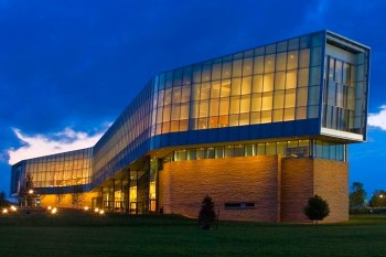 A modern building with glass walls and illuminated interior against a twilight sky.