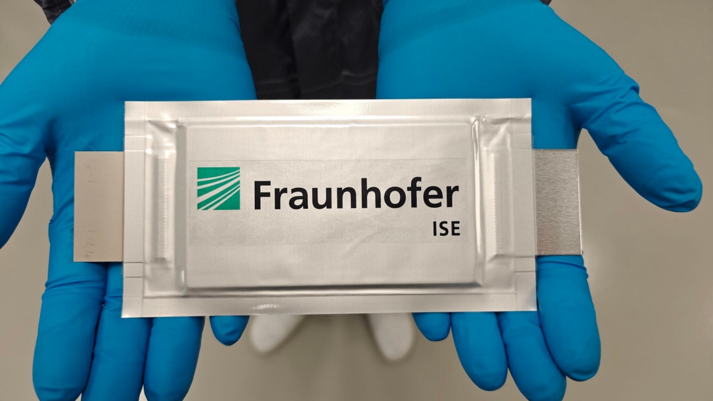 A person wearing blue gloves holds a metallic packaging labeled "Fraunhofer ISE."