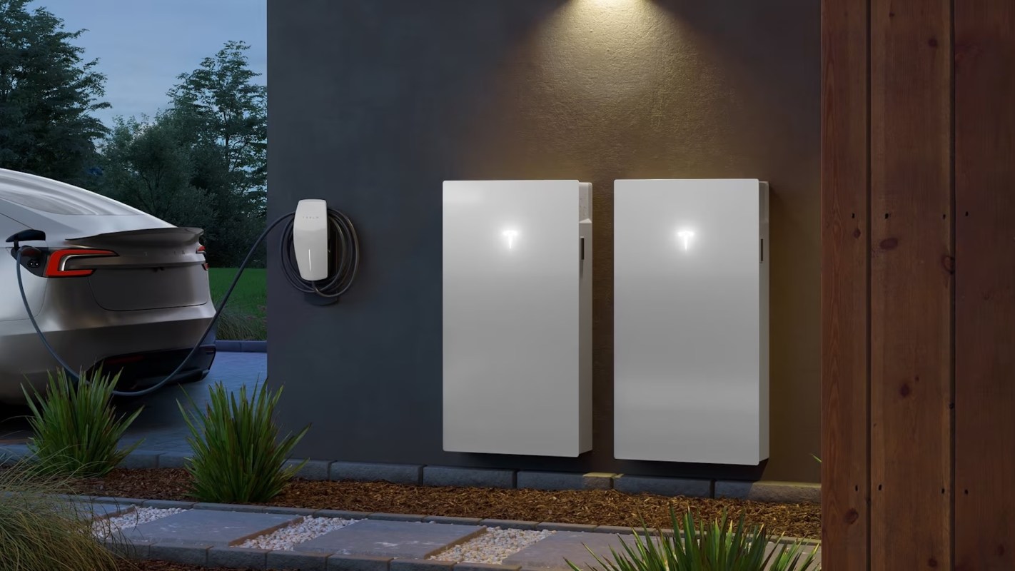 A car parked beside two white Tesla Powerwall storage units and an electric vehicle charger on a wall.