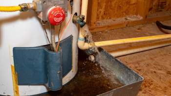 A water heater leaking water into a metal collection pan in a basement.