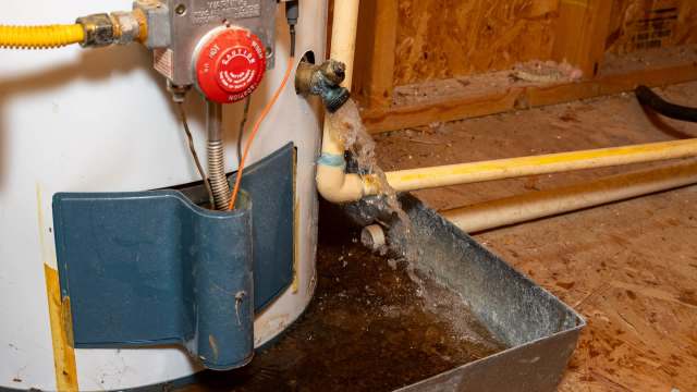 A water heater leaking water into a metal pan.