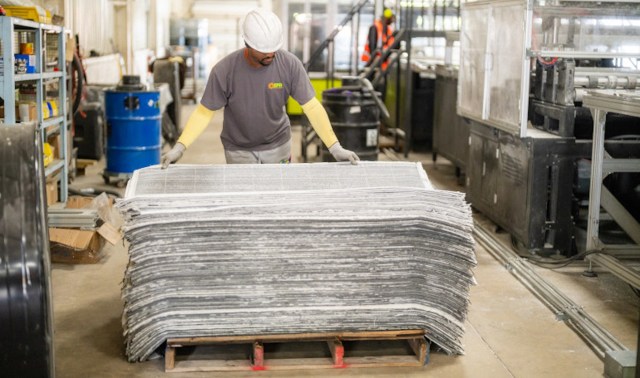 A worker moves a stack of sheets of recycled solar panels in a facility.