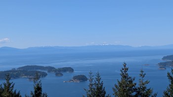 A panoramic view of islands and ocean under a clear blue sky with distant snow-capped mountains.