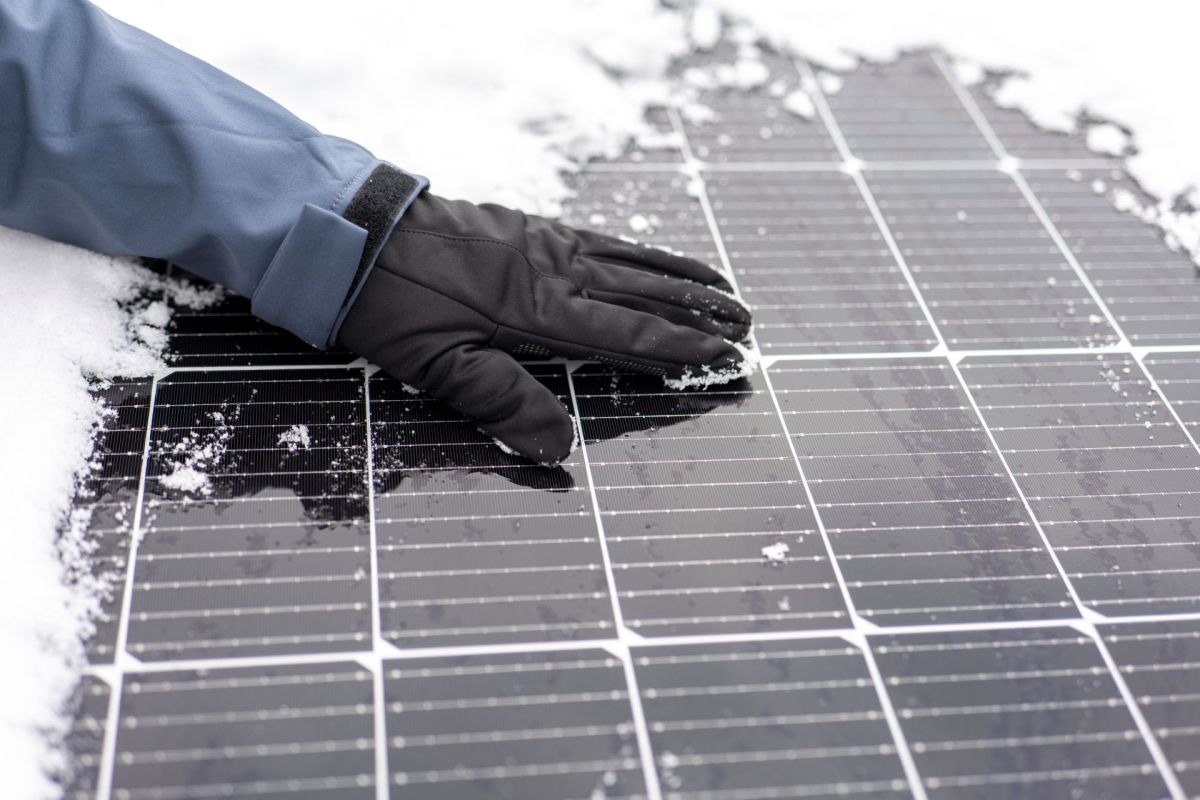 A gloved hand wipes snow off of a solar panel