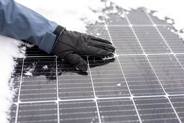 A gloved hand wipes snow off of a solar panel