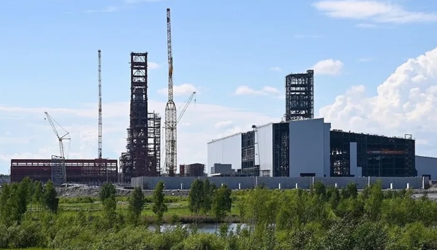 A construction site featuring several tall structures and cranes against a blue sky.