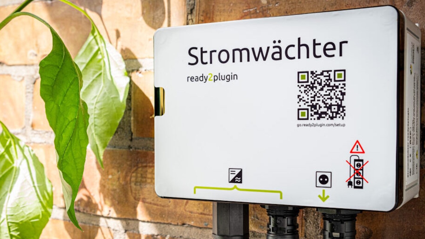 A solar battery mounted on a wall with a QR code and various symbols, surrounded by green leaves.
