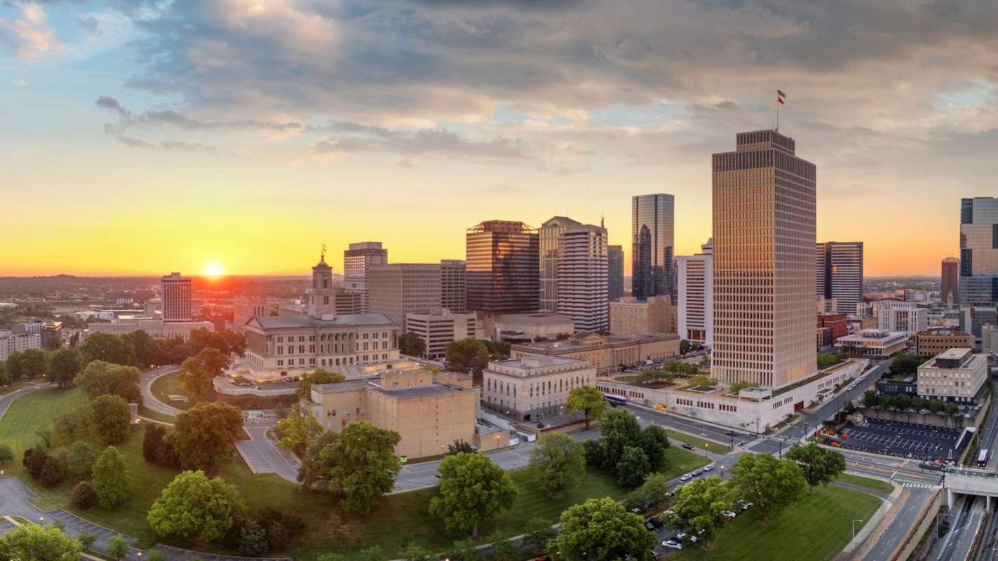 A city skyline at sunset with buildings and greenery in the foreground.