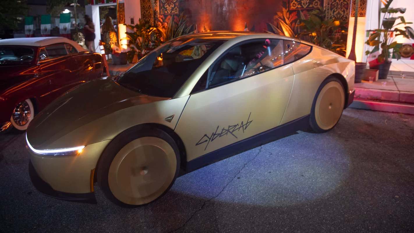 A gold-colored electric Tesla with large wheels and "CYBERCAB" written on the side, parked in an outdoor setting.