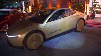 A gold-colored electric Tesla with large wheels and "CYBERCAB" written on the side, parked in an outdoor setting.