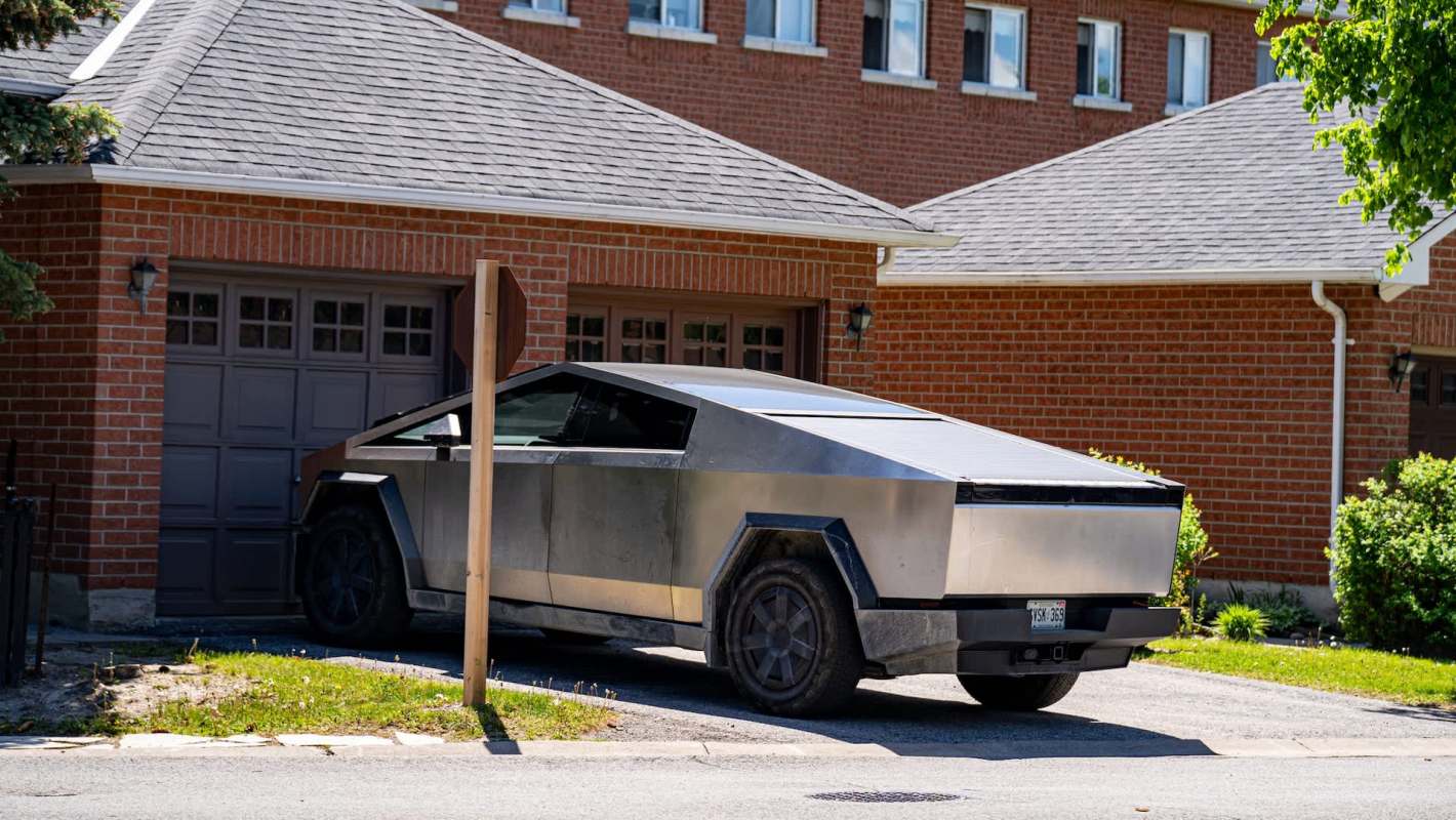 A Tesla Cybertruck parked in a driveway next to a brick house.