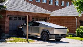 A Tesla Cybertruck parked in a driveway next to a brick house.