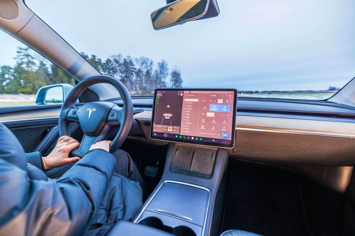 An interior view of a Tesla car, showing the steering wheel and large touchscreen display.