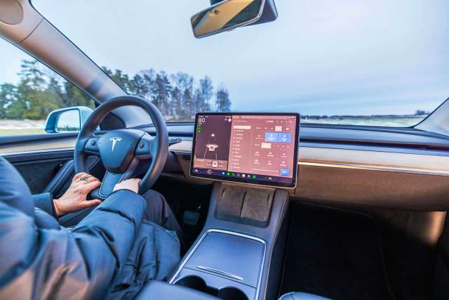 An interior view of a Tesla car, showing the steering wheel and large touchscreen display.