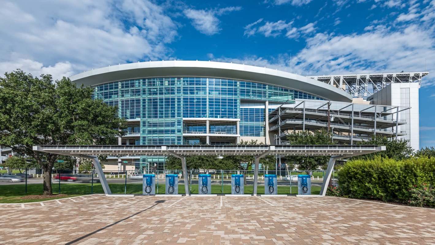 NRG Stadium with glass exterior is visible alongside a row of electric vehicle charging stations.