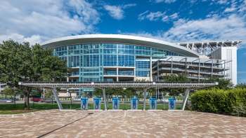 NRG Stadium with glass exterior is visible alongside a row of electric vehicle charging stations.