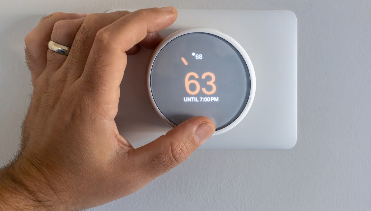 A hand adjusting a smart thermostat displaying a temperature of 63 degrees.