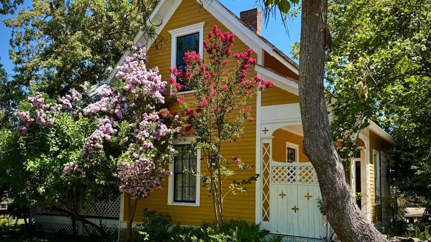 A yellow house with flowers and greenery surrounding it.