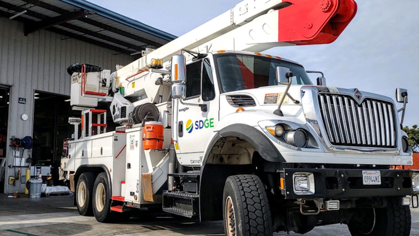 A SDG&E utility truck with a crane and equipment parked in front of a building.