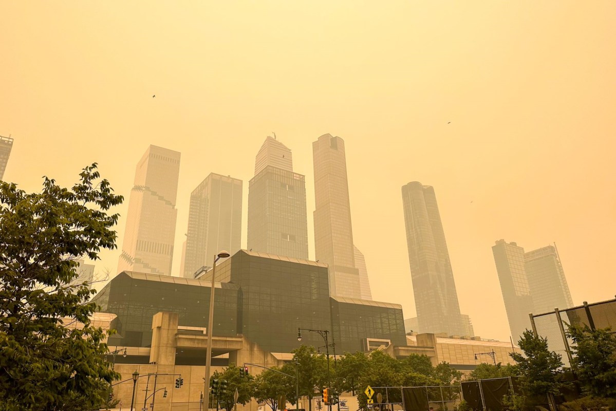 Tall buildings shrouded in hazy, yellow sky with urban greenery in the foreground.