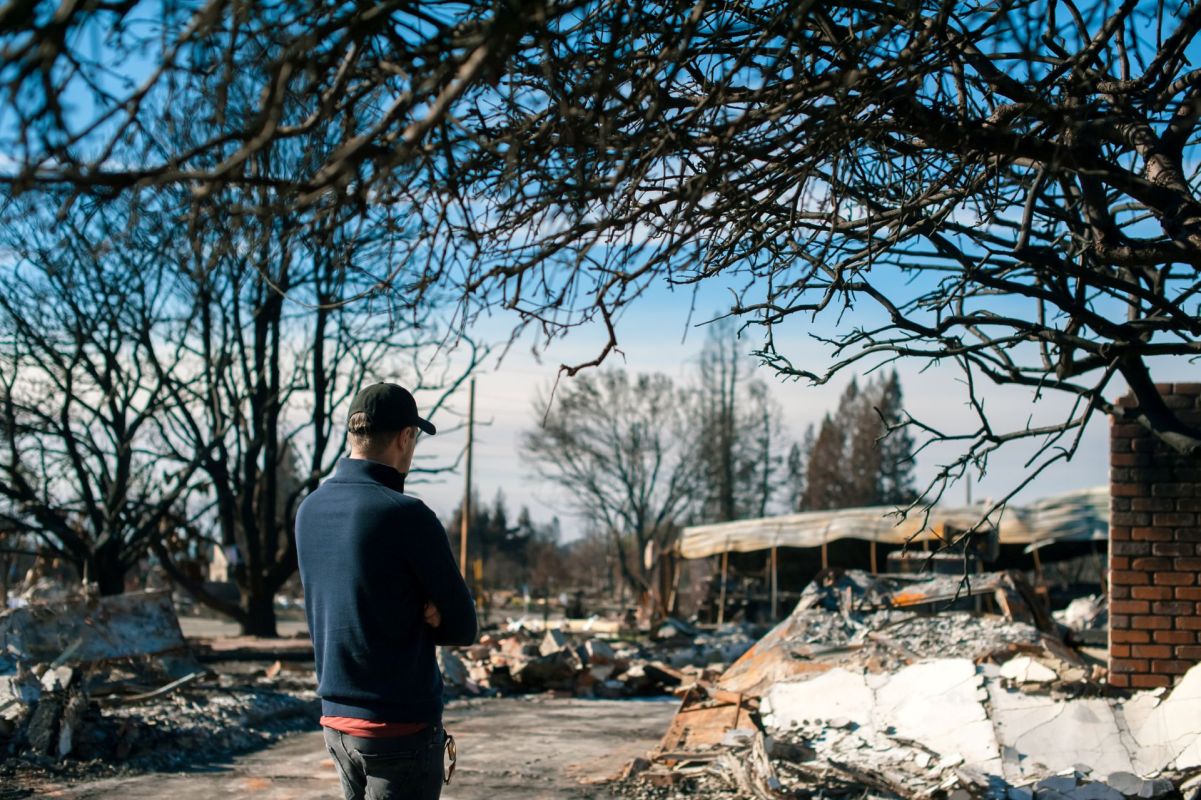 A man surveys the aftermath of a wildfire in a smoldering town