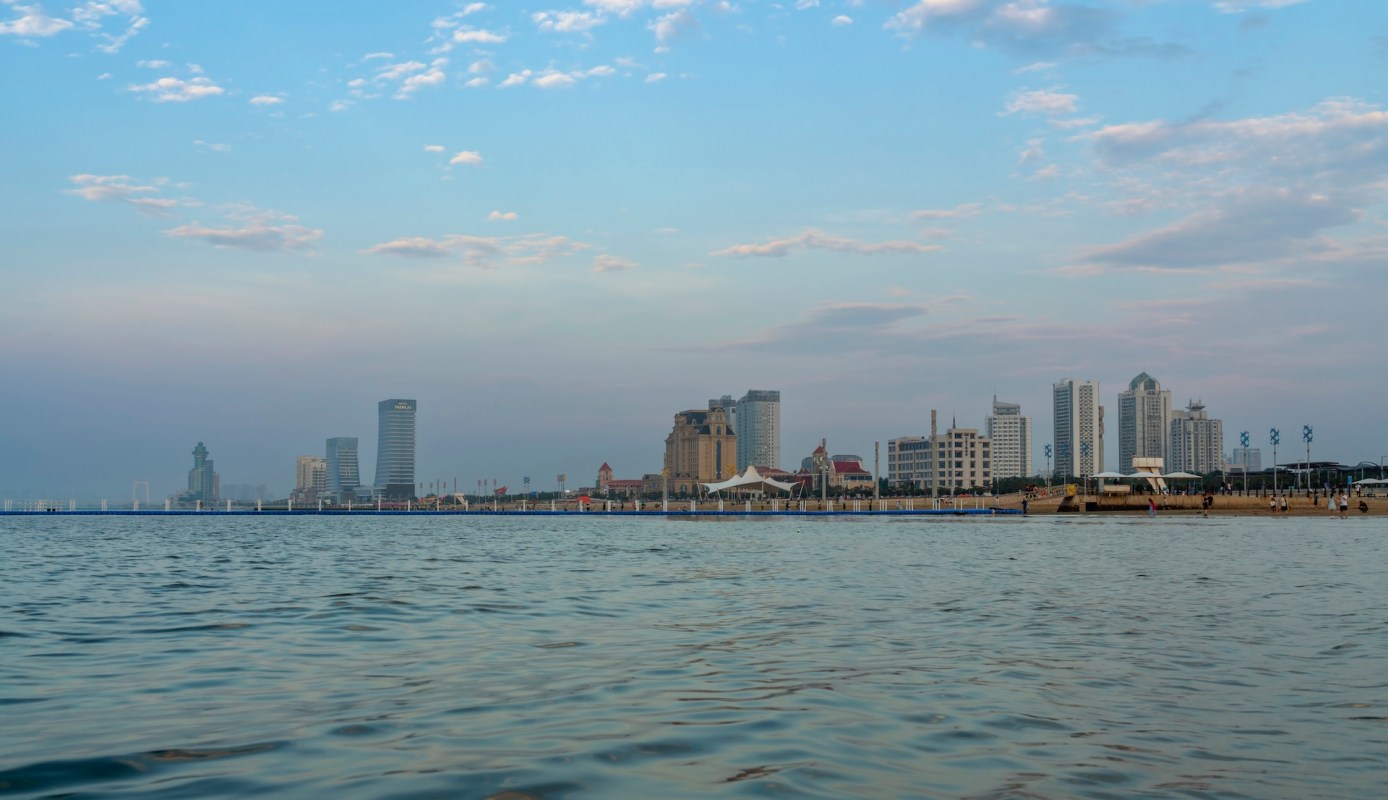 A waterfront view of a city skyline with modern buildings and a beach.