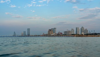 A waterfront view of a city skyline with modern buildings and a beach.