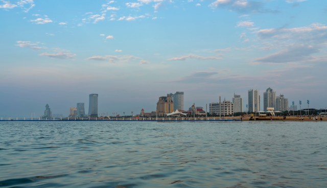 A waterfront view of a city skyline with modern buildings and a beach.