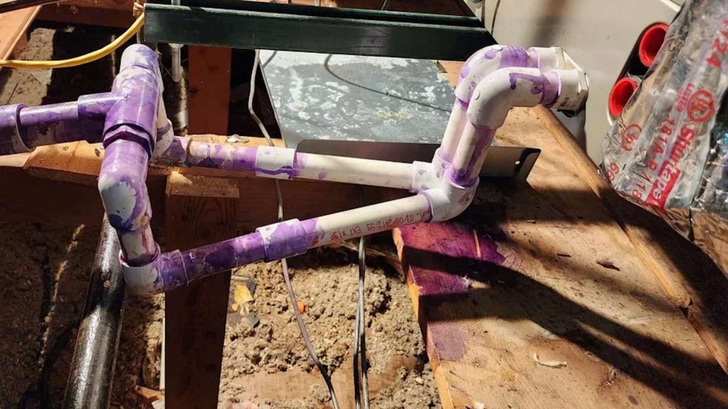A section of purple marked PVC piping on a wooden surface with exposed wires and surrounding materials.