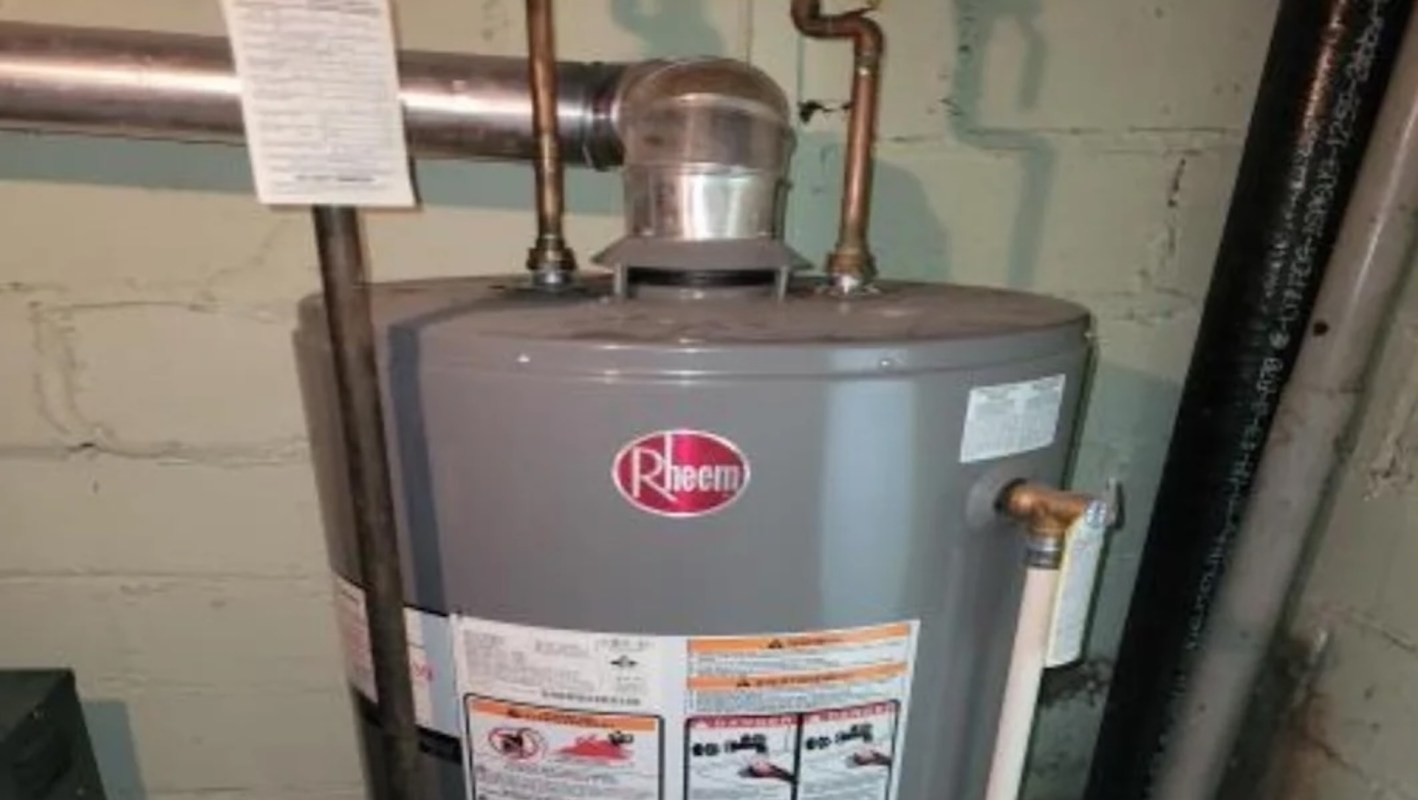 A Rheem water heater with pipes and a warning label in a basement setting.