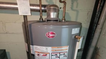 A Rheem water heater with pipes and a warning label in a basement setting.