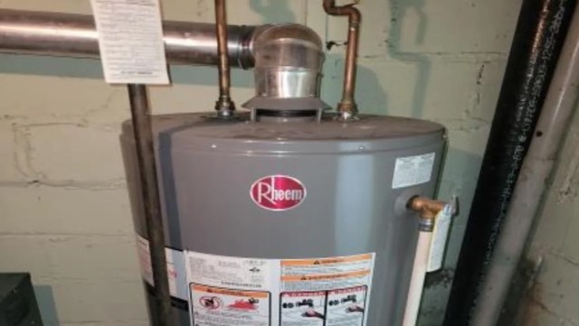 A Rheem water heater with pipes and a warning label in a basement setting.