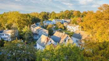 A neighborhood with houses, trees, and a multi-family building under a clear sky.