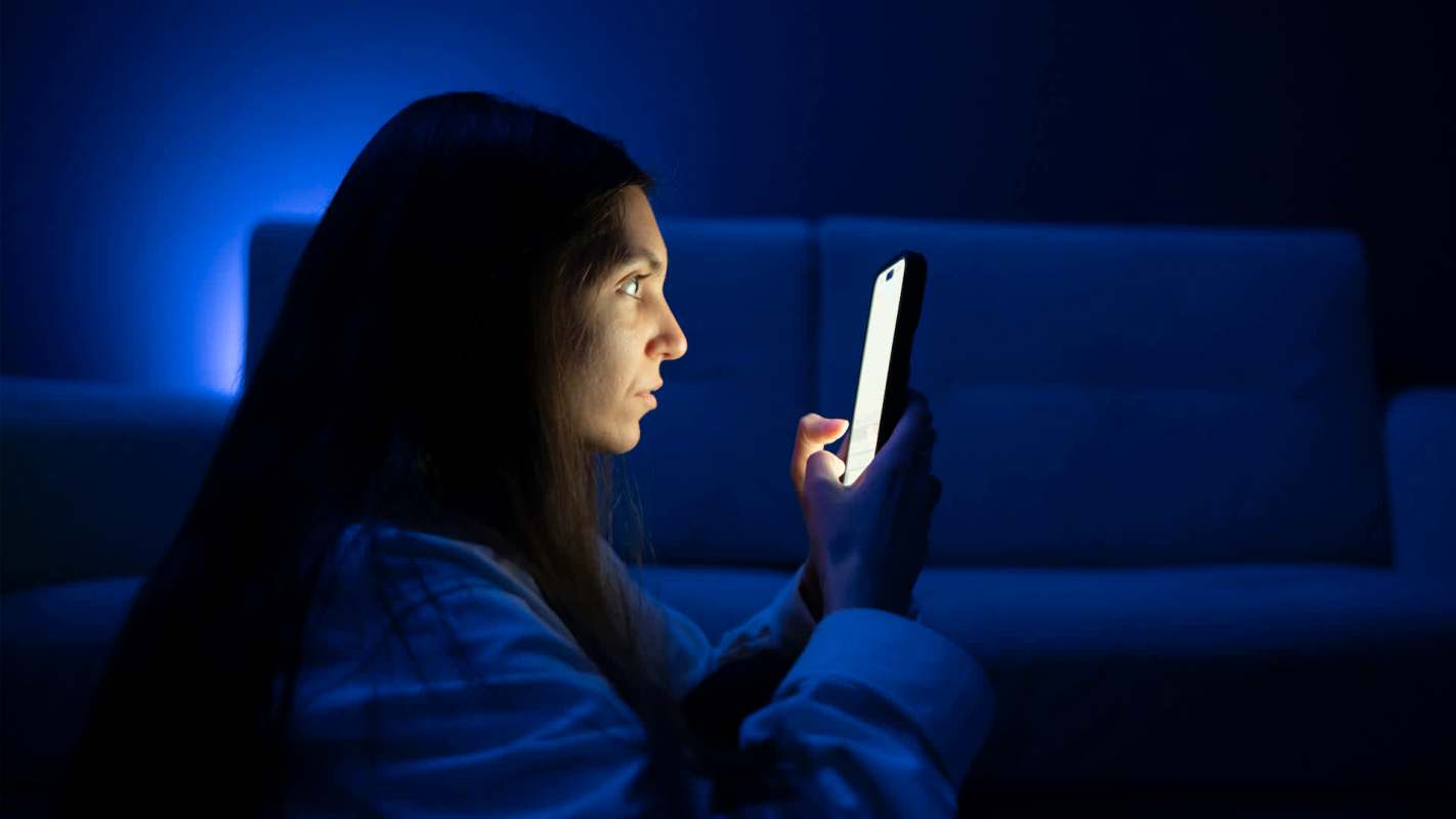 A person staring at a phone in a dark room.