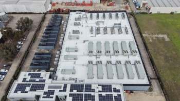 Aerial view of a data center building with rooftop air conditioning units and solar panels, surrounded by vehicles and open space.