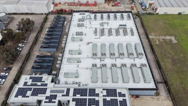 Aerial view of a data center building with rooftop air conditioning units and solar panels, surrounded by vehicles and open space.