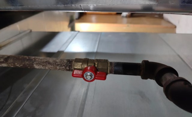 A metal pipe with a red valve attached, positioned against a stainless steel surface.