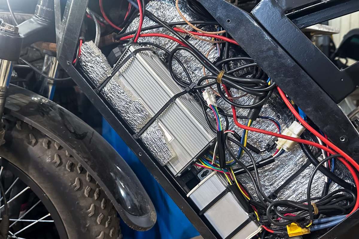 An electric bike's battery compartment filled with wires and components.