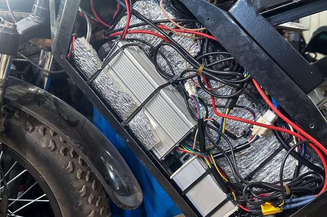 An electric bike's battery compartment filled with wires and components.