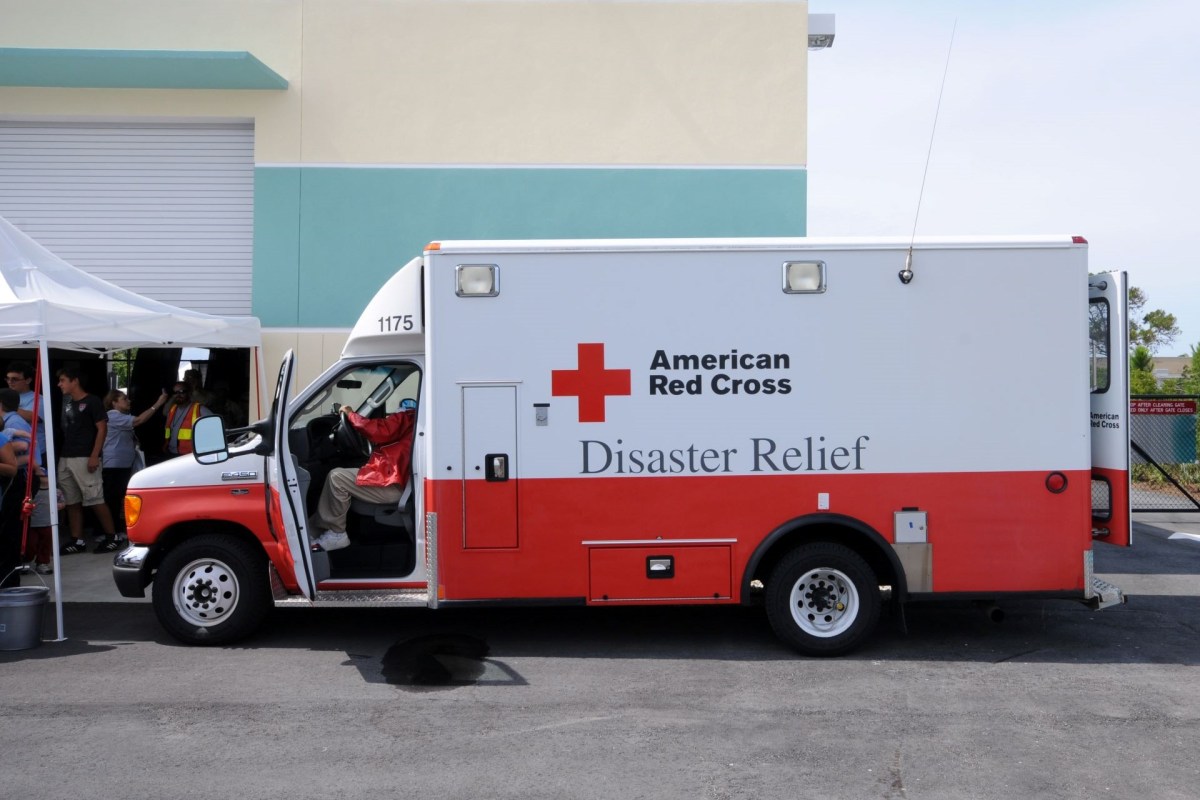 An American Red Cross disaster relief vehicle parked outside a building with people gathering nearby.