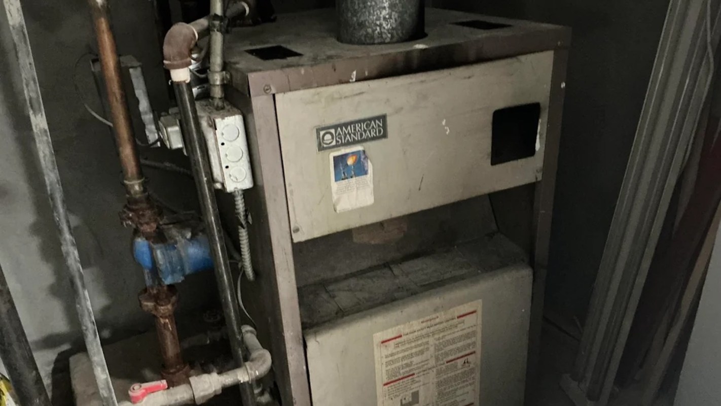 A vintage heating unit with pipes and a control panel in a dimly lit space.