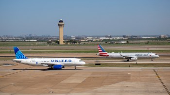 Two airplanes from United and American Airlines taxi on a runway near an airport control tower.
