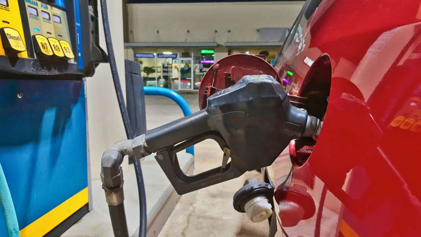 A fuel nozzle inserted into the gas tank of a red vehicle at a gas station.