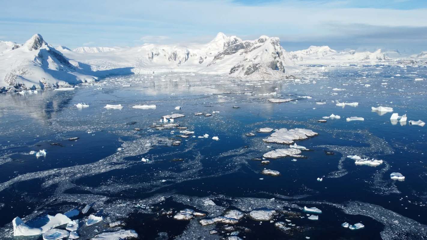 An icy landscape with mountains, floating icebergs, and calm blue water under a clear sky.