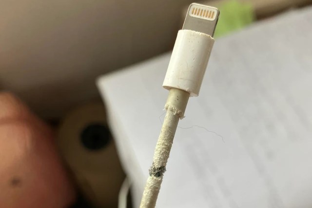 A damaged Lightning charging cable with frayed insulation and exposed wires near the connector.