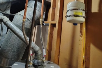 Pipes and a gas detector are installed near a water heater in a basement environment.
